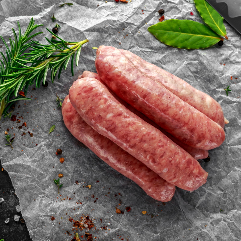 Freshly Made Raw Breed Butchers Sausages In Skins With Herbs On Crumpled Paper